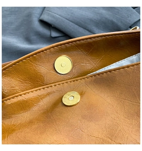 Detailed macro view of the gold magnetic closure and oil wax leather texture on brown handbag
