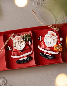 Detail of two hand-painted resin Santa pendants with jute ropes in a red gift box