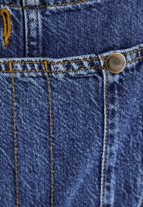 Detail of blue denim overalls showing yellow contrast stitching and vintage metal button