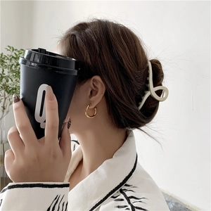 Detail of model wearing gold thick hollow C-shaped hoop earrings and cream hair claw clip