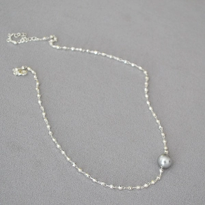 Detail of silver bead necklace featuring a single grey pearl pendant on textured grey cloth