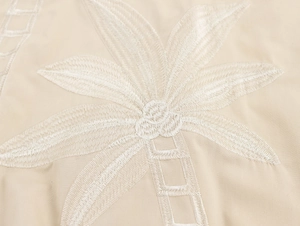 Détail de la broderie cocotier blanc sur tissu beige avec surpiqûres de précision