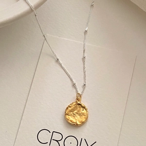 Detail of artistic gold irregular texture pendant with silver satellite beaded chain