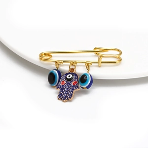 Detailed view of a gold safety pin brooch featuring a blue Hamsa hand and Evil Eye charms