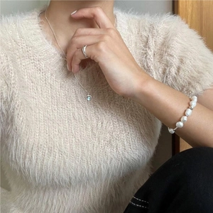 Close-up of S925 silver heart necklace and pearl bracelet worn with a beige sweater
