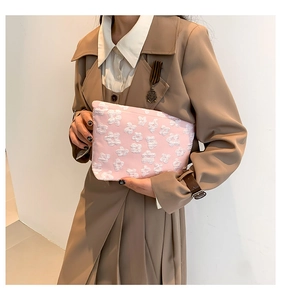 Pink embossed fabric clutch bag with white floral texture held by a model in a trench coat