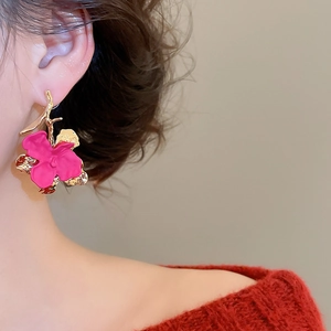 Close-up of a model wearing matte rose red flower earrings with gold metal stems