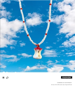 Detail of beaded necklace with a red resin half-bitten apple pendant against a blue sky