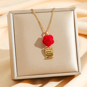 Gold necklace featuring a red velvet rose and an engraved rectangle pendant in a gift box