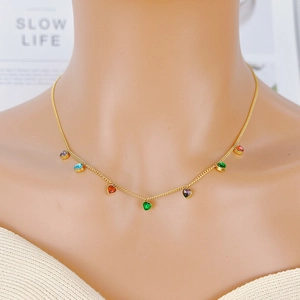 Golden necklace with colorful heart-shaped zircon stones worn by a model in a natural setting