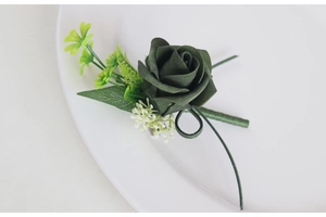 Detail of dark green foam rose boutonniere with baby breath on white ceramic plate