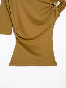 Detail of tan asymmetrical one-shoulder top featuring side pleats and a gold ring accent