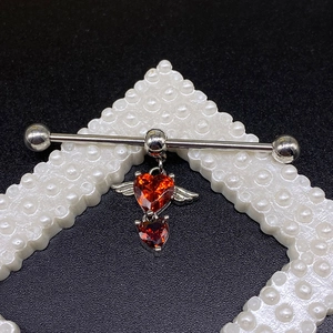 Macro di piercing industriale con zirconi rossi a cuore e ali in metallo dettagliate