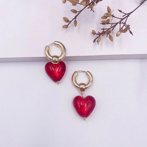 Détail de boucles d'oreilles créoles dorées avec pendentifs en verre cœur rouge vif