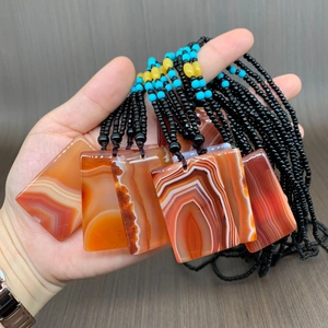 Handheld group of agate pendant necklaces with orange stripes and black beaded strings