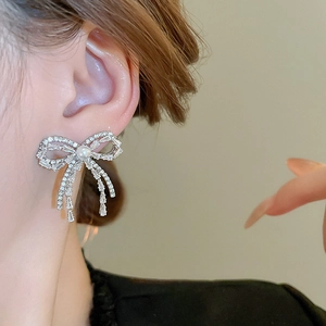 Detail of silver bow earrings with faux pearls and sparkling tassels on model
