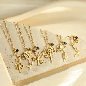 Detail of 18k gold plated birth flower pendants with sparkling gemstones on stone stand
