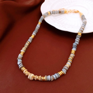 Detail of beaded necklace with gray stones and gold pumpkin charm on red silk