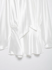 Dettaglio di abito in raso bianco con scollo a fiocco ed eleganti pieghe in vita