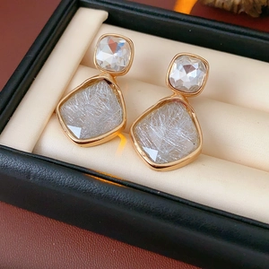 Détail de boucles d'oreilles vintage dorées avec gemmes transparentes sur un écrin beige