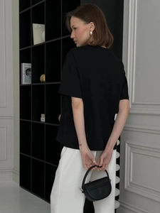 Side view of black oversized cotton t-shirt featuring pearl necklace print in lifestyle setting