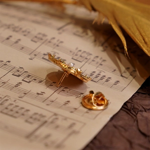 Elegant gold flower brooch with pearls and rhinestones on a vintage music sheet background