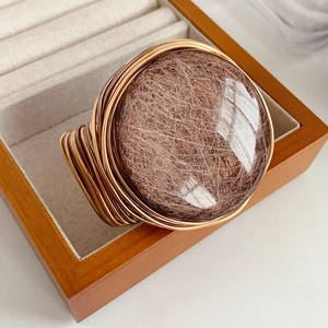Detailed macro view of copper-gold wire wrapped rutilated quartz ring on wood