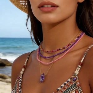 Detail of layered pink crystal and purple hexagonal stone beaded necklaces on beach