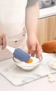 Close-up of a grey silicone spatula mixing flour and eggs in a marble kitchen setting