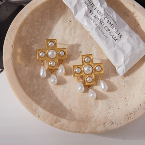 Dettaglio macro di orecchini a croce vintage eleganti con perle e finitura oro