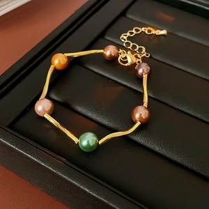 Detailed shot of gold link bracelet with colorful pearls and lobster clasp on black tray