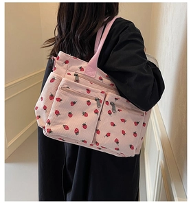 Detail of pink corduroy tote bag with strawberry pattern and zipper pockets worn by model