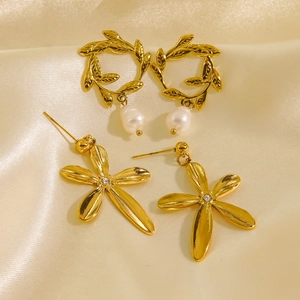 Detailed shot of 14K gold leaf pearl hoops and floral zircon earrings on beige silk fabric