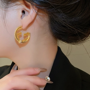 Detail of 18K gold plated F-letter earrings with zircons on a model's ear