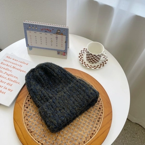 Detail of dark blue and green chunky knit beanie with thick ribbed texture on wooden tray