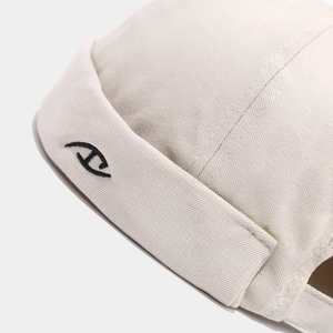 Detail of beige docker hat showing high-density cotton texture and black embroidery