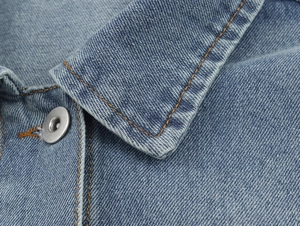 Detail of blue denim fabric showing orange contrast stitching and silver metal buttons