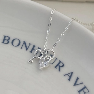 Sterling silver necklace with heart zircon and key charms on white ceramic plate