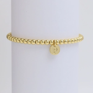 Close-up of golden beaded bracelet featuring a round metal charm with letter P engraving