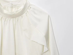 Detail of white satin shirt featuring pleated stand collar and elegant ruffle decoration