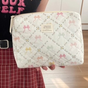 Trousse de maquillage matelassée blanche avec nœuds colorés et fleurs tenue par un modèle