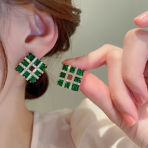 Detailed view of gold square earrings with green gemstones and sparkling zircon stones