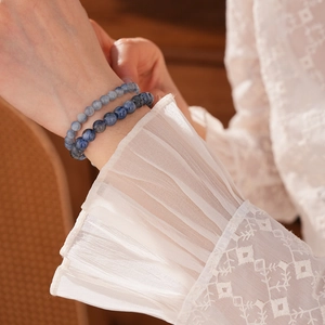 Close-up of blue synthetic kyanite bead bracelets worn with lace sleeve in warm light