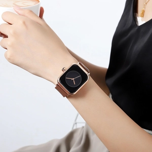 Women's rose gold square watch with brown silicone strap worn on wrist with coffee