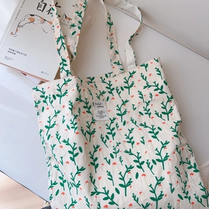 Close-up of floral cotton tote bag with green leaves, orange flowers and brand label