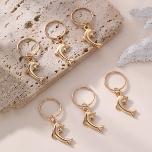 Detailed close-up of golden dolphin hair charms on a beige stone with coral accents