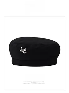 Detailed close-up of a black wool beret with a stylish silver metal cross decoration