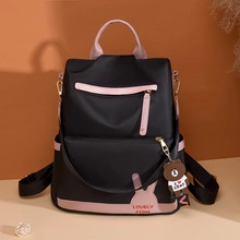Detail of a black nylon backpack featuring pink straps and a decorative bear keychain