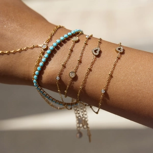 Detail of layered gold bracelets with turquoise beads and pavé heart charm pendants
