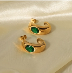 Close-up of 18K gold plated C-shaped earrings with green zircon on golden silk fabric